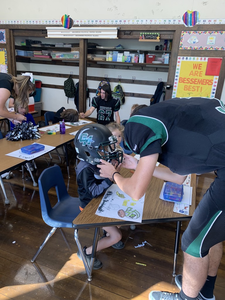 football player helping younger student try on his helmet