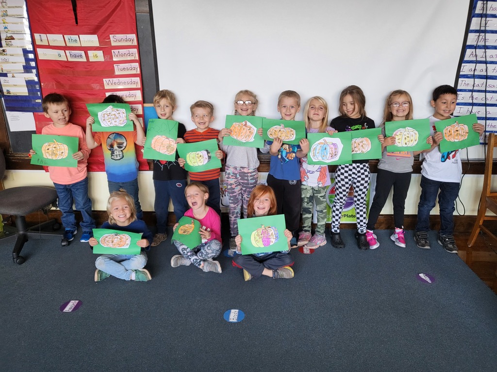 Kindergarten students holding drawings of pumpkins made with seeds