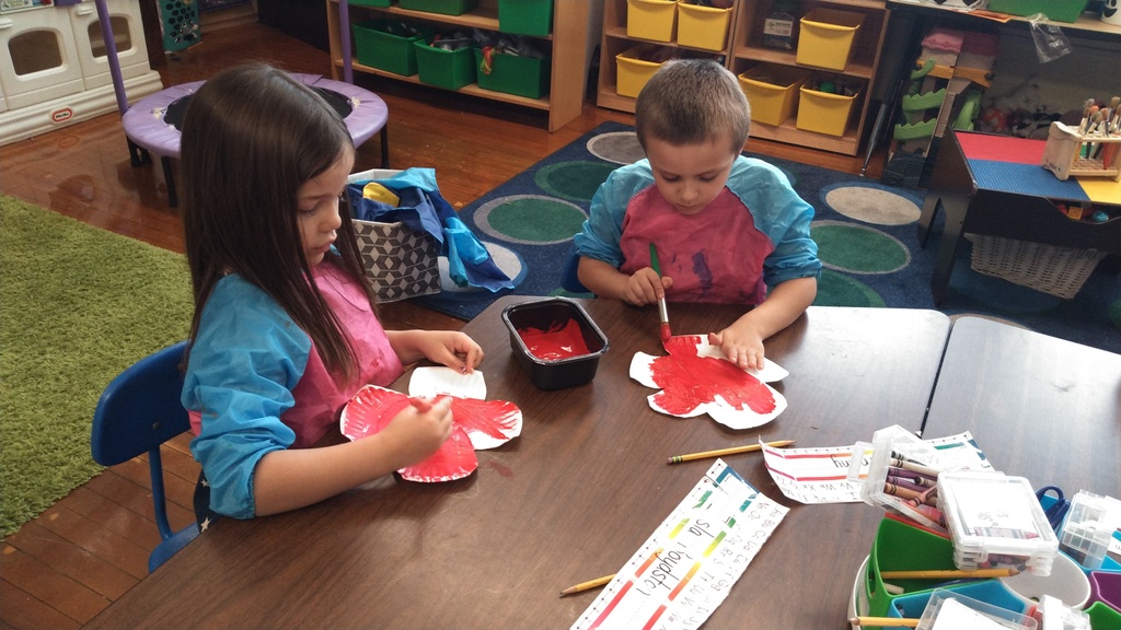 Boy and girl Kindergarten students painting red poppies  on paper plates