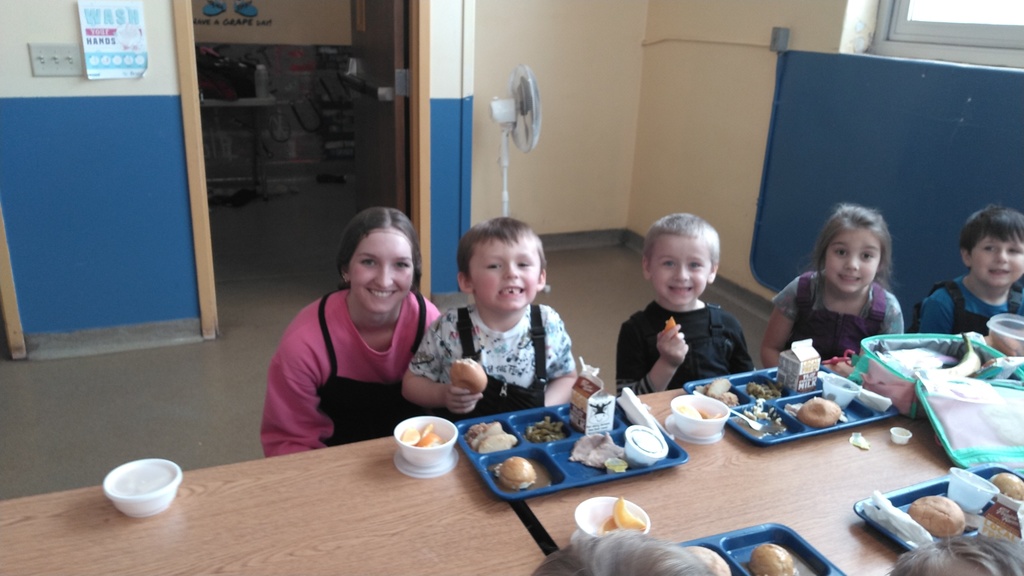 older student posing with younger students eating lunch